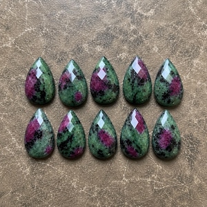 May include: Ten teardrop-shaped cabochons arranged in two rows of five. Each stone features a faceted surface with a mottled pattern of deep green zoisite, vibrant magenta ruby inclusions, and dark black hornblende mineral patches throughout.