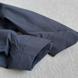 May include: Close-up of a dark navy blue long-sleeve shirt. The image highlights the cuff and sleeve details, showcasing the tailored construction and fabric texture. The shirt appears to be made of a smooth, possibly woven material.