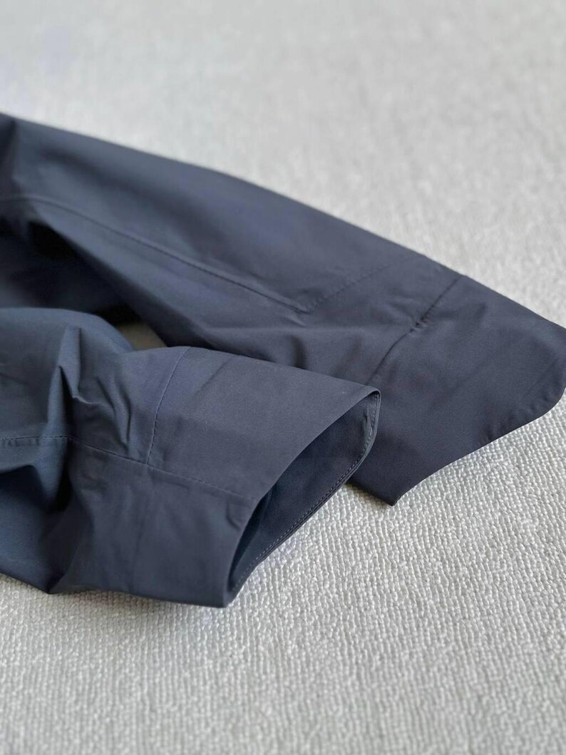 May include: Close-up of a dark navy blue long-sleeve shirt. The image highlights the cuff and sleeve details, showcasing the tailored construction and fabric texture. The shirt appears to be made of a smooth, possibly woven material.