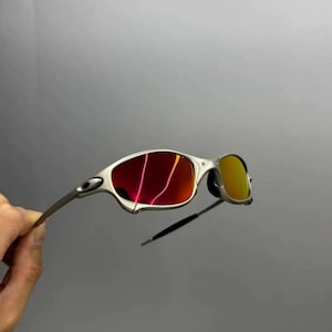 Może przedstawiać: Okulary przeciwsłoneczne w srebrnej oprawie z czerwonymi i ż&oacute;łtymi soczewkami. Okulary przeciwsłoneczne mają elegancki, nowoczesny design z zakrzywioną oprawą i małym, owalnym kształtem soczewek. Soczewki odbijają światło.