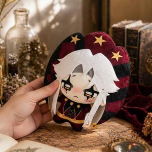 May include: A plush doll with white hair and a red and black outfit. The doll has a sad expression and is held in a hand. The background includes books and decorative items.