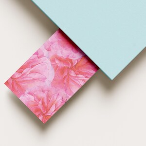 Peut inclure: Une carte rectangulaire ornée d'un motif floral rose vif avec des pétales de rose superposés, partiellement glissée sous un panneau rectangulaire bleu clair uni. La carte présente un motif botanique répétitif dans des tons magenta et rose.