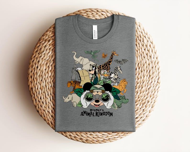Puede incluir: Una camiseta gris jaspeado de cuello redondo con un estampado gr&aacute;fico de Mickey Mouse mirando a trav&eacute;s de binoculares rodeado de varios animales y personajes de Disney, con el texto "Disney's ANIMAL KINGDOM" impreso en negro bajo la ilustraci&oacute;n.