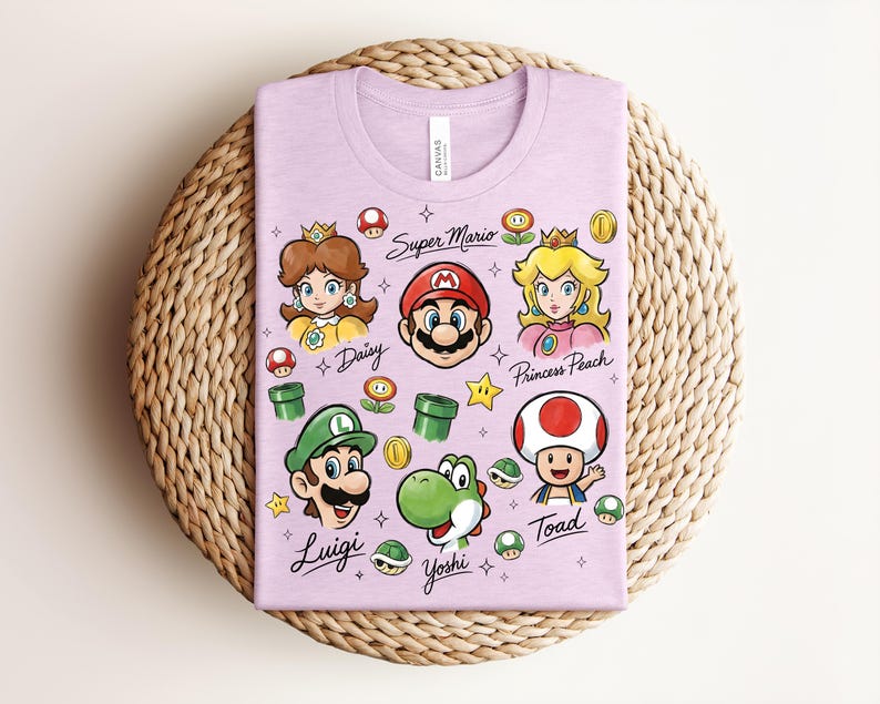 May include: A light purple t-shirt featuring cartoon illustrations of Super Mario characters, including Mario, Luigi, Princess Peach, and Yoshi. The words "Super Mario" and character names are printed on the shirt.