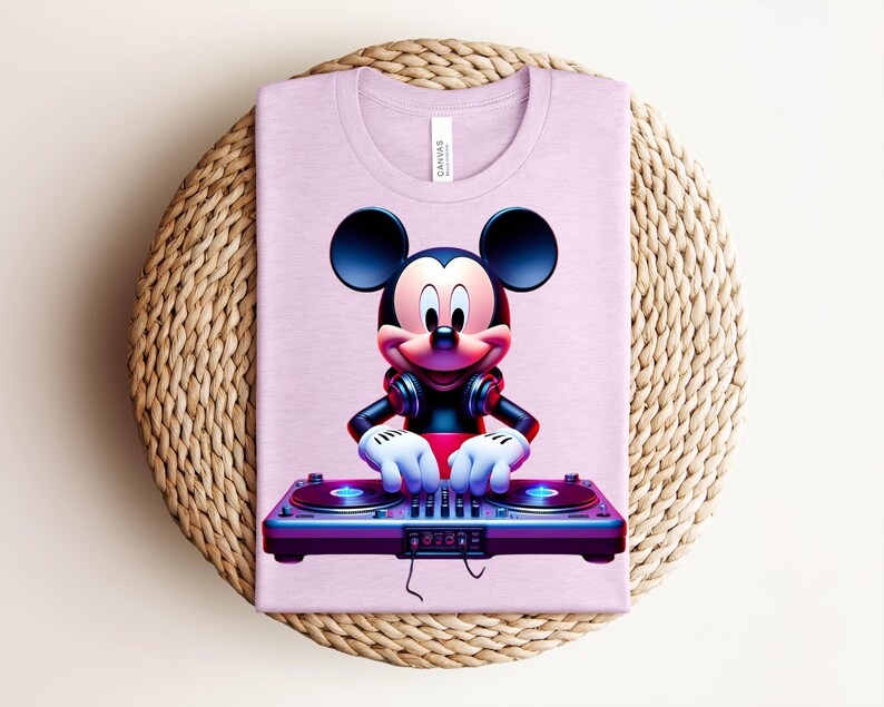 May include: A light purple t-shirt featuring a graphic of Mickey Mouse as a DJ. Mickey is wearing headphones and has his hands on a DJ mixer. The shirt is folded on a woven, circular placemat.