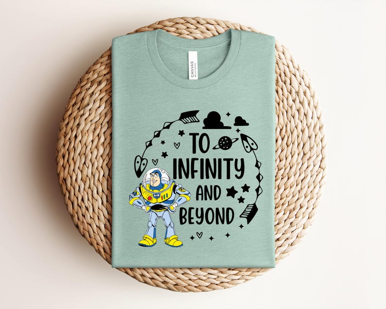 Puede incluir: Una camiseta verde claro con un gr&aacute;fico de un personaje de guardi&aacute;n espacial con traje blanco, azul y amarillo. El texto "TO INFINITY AND BEYOND" aparece en negro, rodeado de ilustraciones negras de flechas, estrellas, nubes y un planeta.