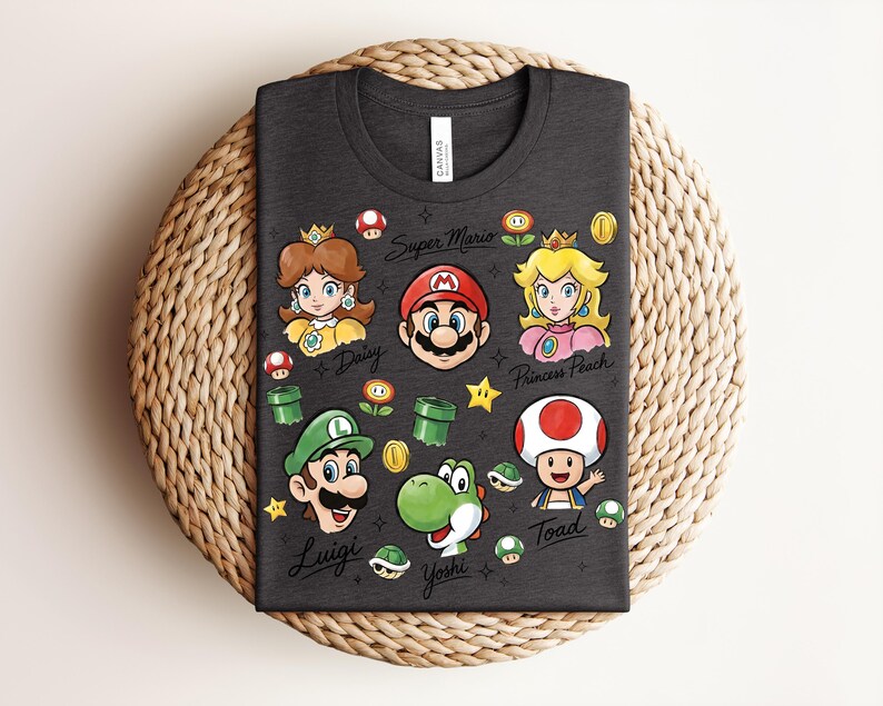May include: Dark gray t-shirt featuring colorful illustrations of Super Mario characters, including Mario, Luigi, Princess Peach, Daisy, Yoshi, and Toad. The words "Super Mario" and character names are also printed on the shirt.