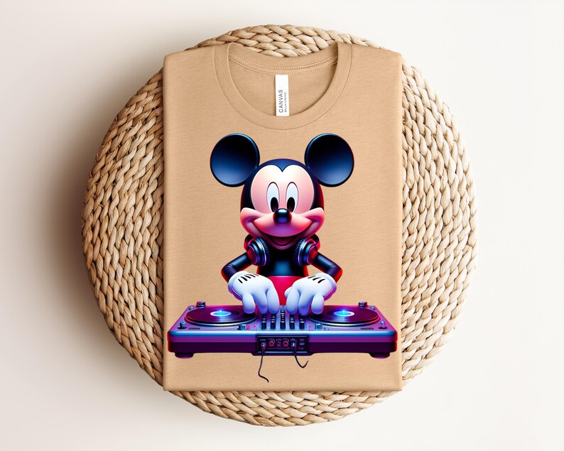 May include: Tan t-shirt featuring a graphic of Mickey Mouse as a DJ, wearing headphones and operating a turntable. The design is vibrant with red, blue, and purple hues. The shirt is folded on a woven, circular surface.