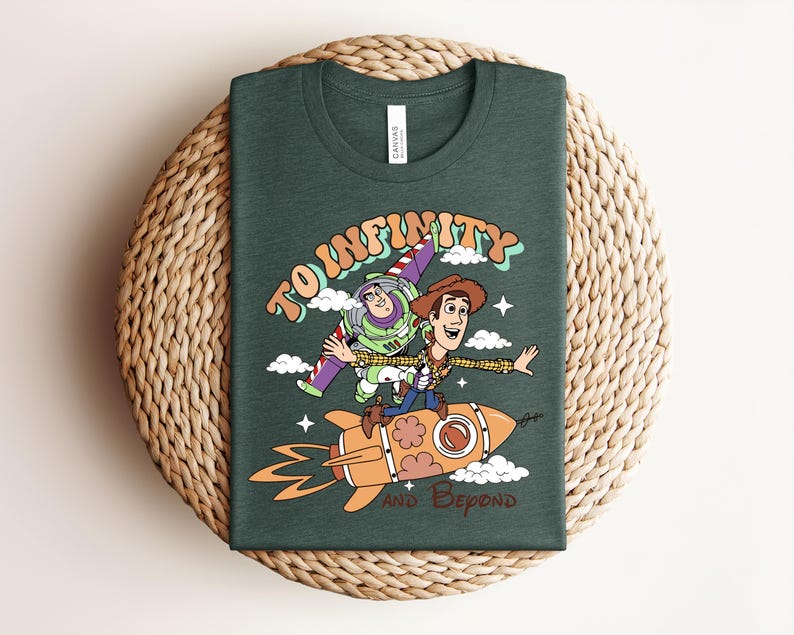 May include: A dark green t-shirt featuring a graphic print of Buzz Lightyear and Woody riding a rocket. The text reads TO INFINITY AND BEYOND in a retro font style. The design includes small white clouds and stars surrounding the characters.