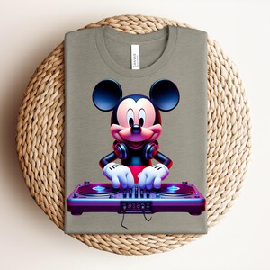 May include: A folded olive green t-shirt featuring a vibrant graphic of Mickey Mouse as a DJ. Mickey is wearing headphones and has his hands on a colorful DJ mixer. The shirt is displayed on a woven, circular placemat.