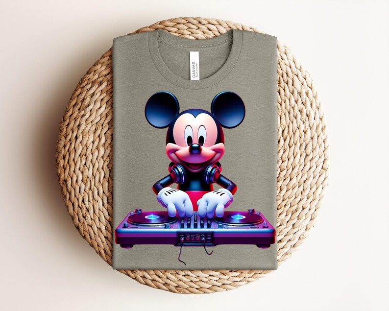 May include: A folded olive green t-shirt featuring a vibrant graphic of Mickey Mouse as a DJ. Mickey is wearing headphones and has his hands on a colorful DJ mixer. The shirt is displayed on a woven, circular placemat.