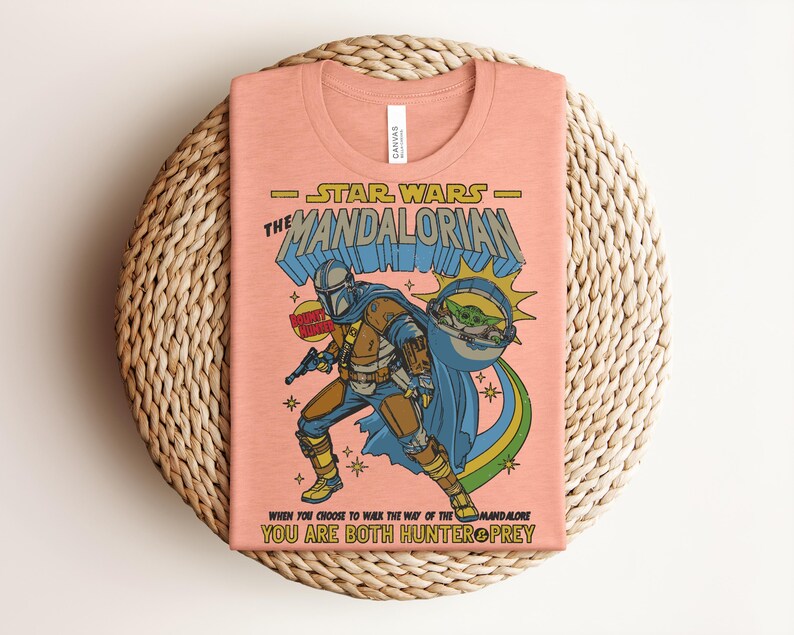 Puede incluir: Una camiseta color melocot&oacute;n con un gr&aacute;fico de The Mandalorian y Grogu. El texto dice STAR WARS THE MANDALORIAN, BOUNTY HUNTER y WHEN YOU CHOOSE TO WALK THE WAY OF THE MANDALORE YOU ARE BOTH HUNTER & PREY. El dise&ntilde;o utiliza colores azul, amarillo y verde.