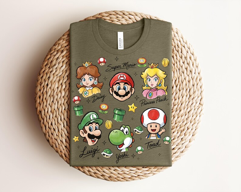 May include: Olive green t-shirt featuring cartoon illustrations of Super Mario characters, including Mario, Luigi, Princess Peach, Daisy, Yoshi, and Toad. The words "Super Mario" and character names are written on the shirt.