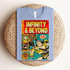 Puede incluir: Una camiseta azul claro con un gr&aacute;fico de portada de c&oacute;mic titulado Infinity & Beyond. El dise&ntilde;o incluye ilustraciones de Buzz Lightyear, el Emperador Zurg y Zurgbot, con elementos de texto en amarillo y rojo y un estilo de c&oacute;mic vintage.