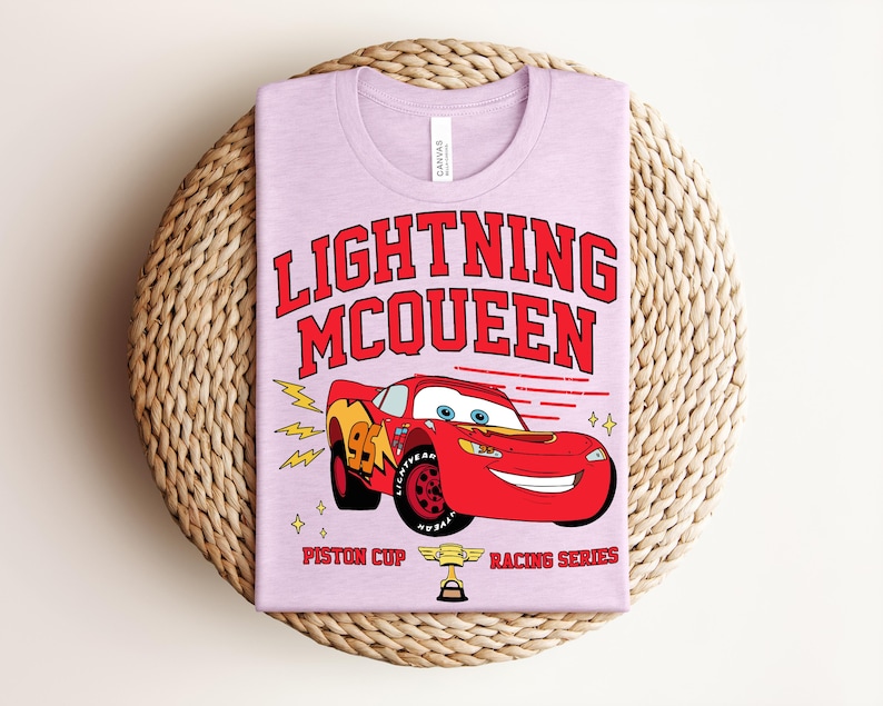 May include: A light purple t-shirt featuring a graphic of Lightning McQueen from the movie Cars. The design includes the text "LIGHTNING McQUEEN" in red, the number 95, and the words "Piston Cup Racing Series".
