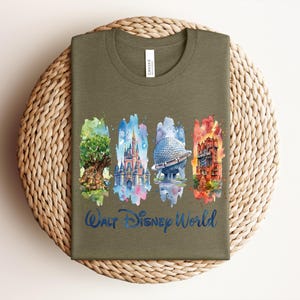 May include: Olive green t-shirt featuring watercolor illustrations of iconic Walt Disney World landmarks. The design includes the Tree of Life, Cinderella Castle, Spaceship Earth, and the Tower of Terror, with "Walt Disney World" in blue script.
