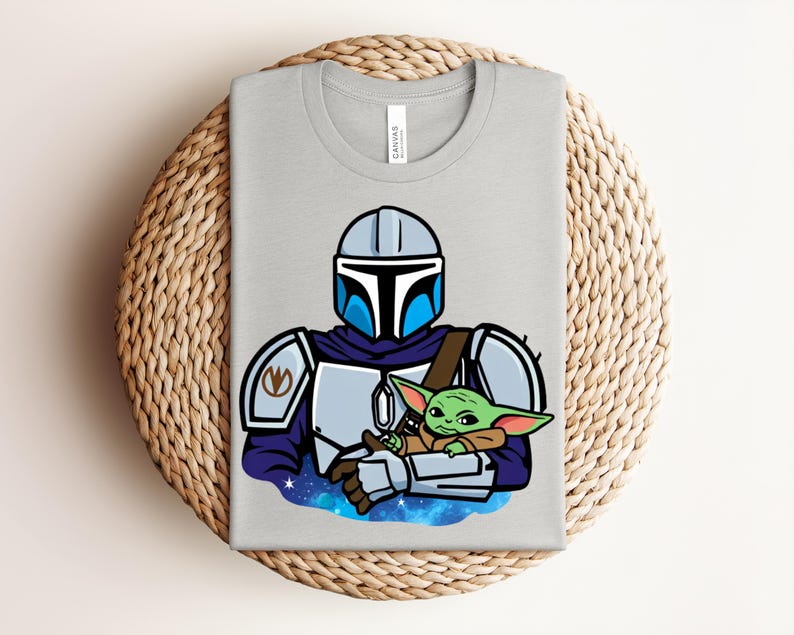 Puede incluir: Una camiseta gris claro con una ilustraci&oacute;n de dibujos animados de un personaje mandaloriano sosteniendo a un alien&iacute;gena verde. El mandaloriano lleva un casco y una armadura con detalles azules y plateados. El alien&iacute;gena es peque&ntilde;o y verde, con orejas grandes.