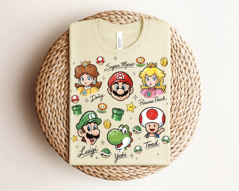 May include: A light tan t-shirt featuring Super Mario characters: Daisy, Mario, Princess Peach, Luigi, Yoshi, and Toad. The shirt includes the text "Super Mario" and character names. The design incorporates stars, mushrooms, and coins.