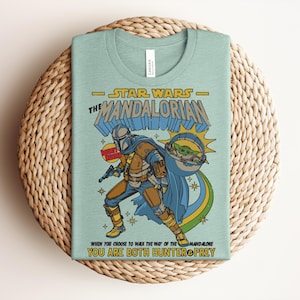 Puede incluir: Una camiseta de color verde claro con un gr&aacute;fico de The Mandalorian y Grogu. El texto dice Star Wars The Mandalorian, Bounty Hunter y When You Choose To Walk The Way Of The Mandalore You Are Both Hunter & Prey. El dise&ntilde;o incluye estrellas.