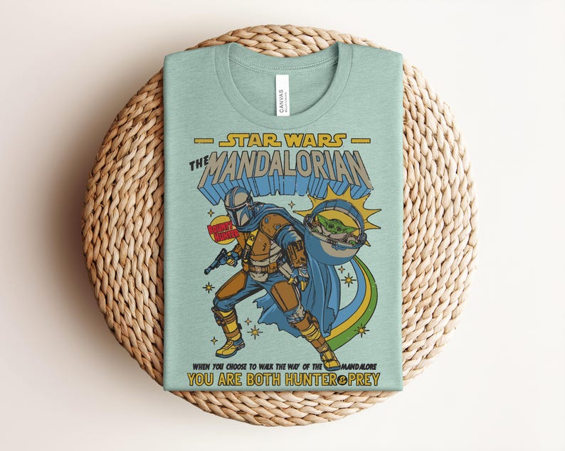 Puede incluir: Una camiseta de color verde claro con un gr&aacute;fico de The Mandalorian y Grogu. El texto dice Star Wars The Mandalorian, Bounty Hunter y When You Choose To Walk The Way Of The Mandalore You Are Both Hunter & Prey. El dise&ntilde;o incluye estrellas.