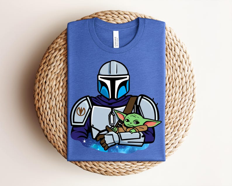 Puede incluir: Una camiseta azul con una ilustraci&oacute;n de dibujos animados de un personaje con armadura plateada que sostiene una peque&ntilde;a criatura verde. El dise&ntilde;o incluye un casco, una armadura para los hombros y una capa. La peque&ntilde;a criatura tiene orejas grandes y est&aacute; envuelta en una manta marr&oacute;n.