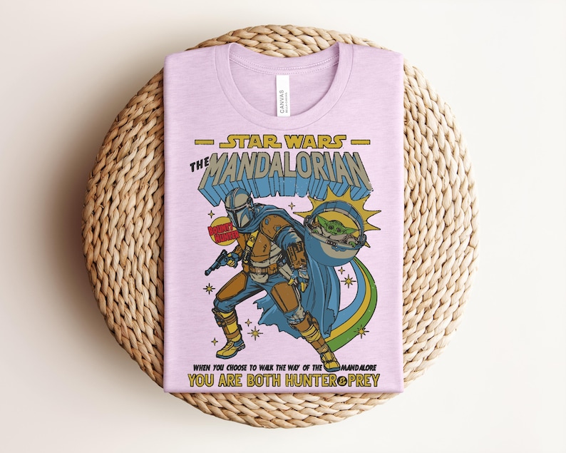 Puede incluir: Una camiseta de color morado claro con un estampado gr&aacute;fico de The Mandalorian y Grogu. El texto dice STAR WARS THE MANDALORIAN, BOUNTY HUNTER y WHEN YOU CHOOSE TO WALK THE WAY OF THE MANDALORE YOU ARE BOTH HUNTER & PREY en amarillo y azul.
