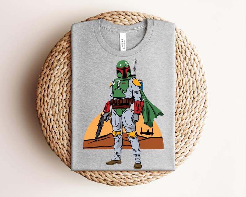 May include: A gray t-shirt featuring a graphic of a Star Wars character, Boba Fett, in his signature green and gray armor, holding a blaster. The design includes a desert landscape and a spaceship silhouette.