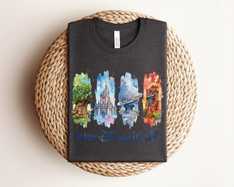 May include: Dark gray t-shirt featuring a watercolor design of four iconic Disney World landmarks: the Tree of Life, Cinderella Castle, Spaceship Earth, and the Tower of Terror. The words "Walt Disney World" are written in blue script below the images. The shirt is folded on a woven mat.