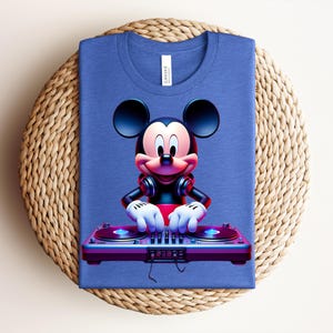 May include: A blue t-shirt featuring a cartoon Mickey Mouse DJ design. Mickey is wearing headphones and has his hands on a DJ mixer. The shirt is folded on a woven, circular placemat.