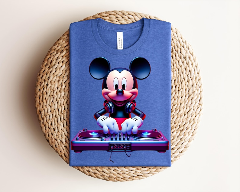 May include: A blue t-shirt featuring a cartoon Mickey Mouse DJ design. Mickey is wearing headphones and has his hands on a DJ mixer. The shirt is folded on a woven, circular placemat.