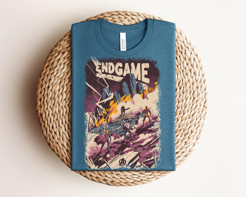 Pu&ograve; includere: Una t-shirt blu a girocollo con una stampa grafica che riporta il testo ENDGAME. L'illustrazione raffigura una scena di battaglia con figure stilizzate, fulmini e fuoco in tonalit&agrave; viola, arancione e bianco, con un logo Avengers in basso.