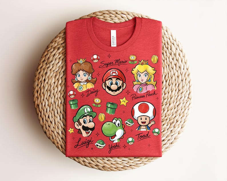 May include: Red t-shirt featuring cartoon characters from Super Mario. The design includes Mario, Princess Peach, Luigi, Yoshi, Toad, and Daisy, along with game-related icons. The words "Super Mario" and character names are also printed on the shirt.