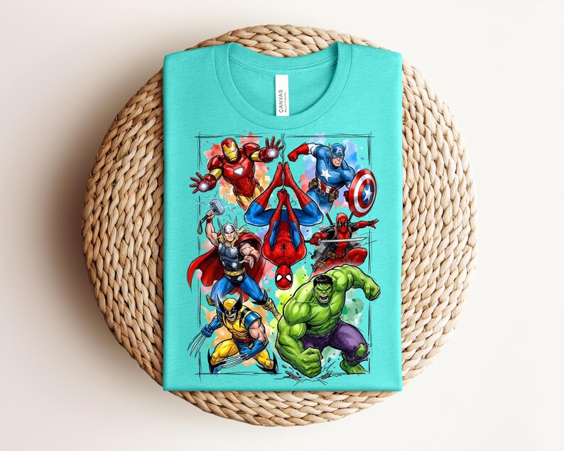 May include: A turquoise t-shirt with a vibrant graphic of superheroes such as Iron Man, Captain America, Spider-Man, Thor, Wolverine, Hulk, and Deadpool. The shirt is folded on a woven, circular surface.