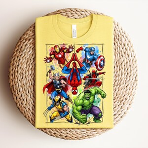 May include: A folded yellow t-shirt with a vibrant graphic of superheroes such as Iron Man, Captain America, and Spider-Man. The design is framed within a rectangle. The shirt rests on a circular woven mat, providing a contrasting texture.