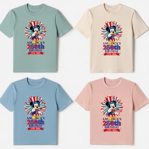May include: Four t-shirts in different colors: green, beige, blue, and pink. Each shirt features a graphic of a cartoon mouse wearing a patriotic hat and holding a flag. The text on the shirts reads "America's 250th Birthday 1776-2026."