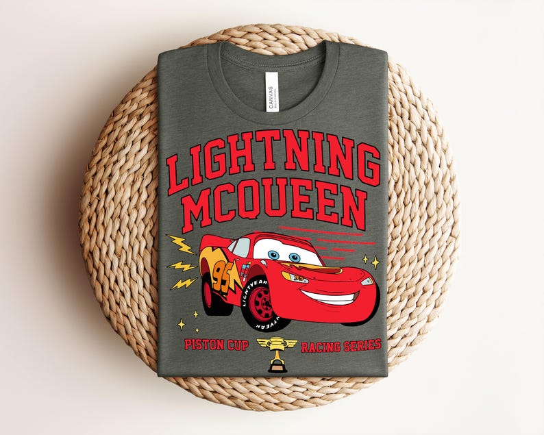 May include: A dark gray t-shirt featuring Lightning McQueen from the Cars movie. The red graphic includes the text "LIGHTNING MCQUEEN" above a red race car with the number 95. Below the car are the words "Piston Cup Racing Series".