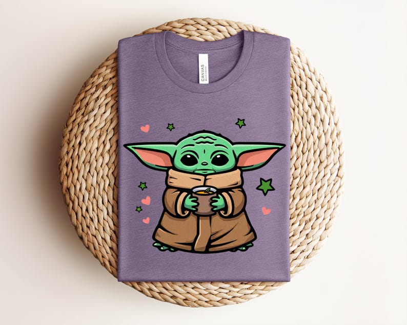 May include: A purple t-shirt featuring a cartoon character holding a cup. The character has green skin, large ears, and is wearing a brown cloak. Pink hearts and green stars are scattered around the character.