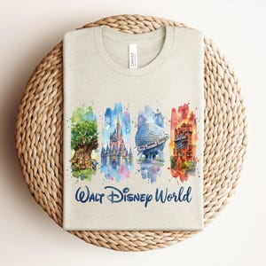May include: A light beige t-shirt featuring a watercolor design of Walt Disney World landmarks. The design includes the Tree of Life, Cinderella Castle, Spaceship Earth, and the Tower of Terror, with "Walt Disney World" written below.