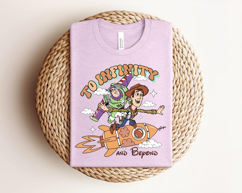 May include: A light purple t-shirt featuring a graphic print of Buzz Lightyear and Woody riding a rocket. The text reads TO INFINITY AND BEYOND in a retro font. The design includes clouds, stars, and orange flames coming from the rocket ship.