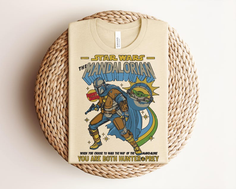 Puede incluir: Una camiseta de color crema con un gr&aacute;fico de The Mandalorian y Grogu. El dise&ntilde;o incluye el texto "Star Wars The Mandalorian", "Bounty Hunter" y "When you choose to walk the way of the Mandalore you are both hunter & prey."