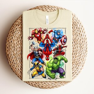 May include: A beige t-shirt with a vibrant graphic of Marvel superheroes, such as Iron Man, Captain America, Spider-Man, Thor, Wolverine, Hulk, and Deadpool. The design is framed with a watercolour effect.