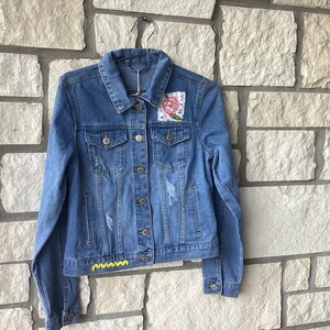 Giacca di jeans nuova, azzurra, con fiori e pizzo (taglia M).