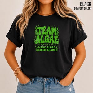 May include: A black short-sleeved t-shirt featuring a bright green graphic print on the chest. The text reads "TEAM ALGAE" above "MAKE ALGAE GREAT AGAIN!" with stylised seaweed and bubble illustrations surrounding the bold, wavy green lettering.