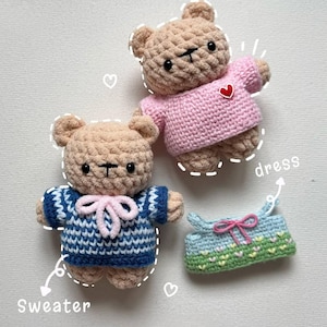 May include: Handmade crocheted teddy bears, one in a pink sweater with a red heart, the other in a blue and white sweater with a pink bow. A small blue, green, and pink dress is also included.