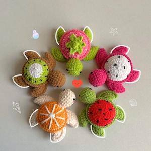 May include: A collection of five crocheted turtles, each designed to resemble a different fruit. The turtles feature a kiwi, strawberry, dragon fruit, orange, and watermelon design. The turtles are in various colors, including green, pink, brown, and white.