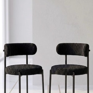 Peut inclure: Deux chaises noires rembourrées au design minimaliste. Les chaises ont un dossier et une assise arrondis, soutenus par de fins pieds en métal noir. Les chaises sont posées sur un sol en marbre blanc.