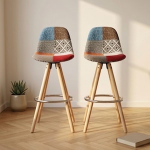 May include: Two bar stools with light wood legs and a footrest. The seats are upholstered with a patchwork design in blue, brown, red, and white. The stools are set against a neutral wall.