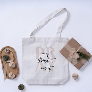 May include: Cream tote bag with the words "Pray on it, through it, over it" in black and tan lettering. A wrapped gift with a ribbon and greenery, and decorative paper balls are also present.