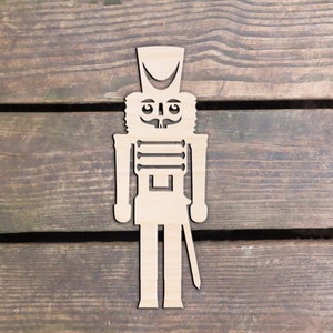May include: A wooden cutout of a nutcracker soldier. The nutcracker is wearing a hat and has a mustache and a sword.