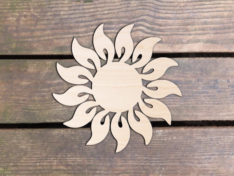 May include: A wooden sun cutout with a decorative design. The sun is made of light brown wood and has a circular shape with a detailed, intricate design around the edge.